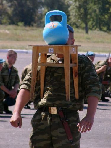 Русский солдат поднимает зубами гирю, стоящую на стуле